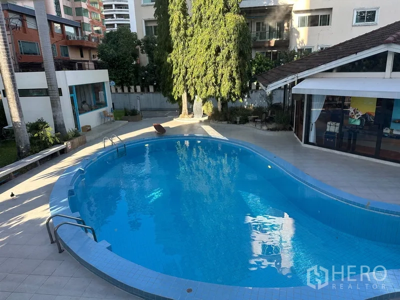 Retail Space for rent in Khlong Toei, Bangkok - Curved swimming pool with tiled deck surrounded by trees and nearby buildings.