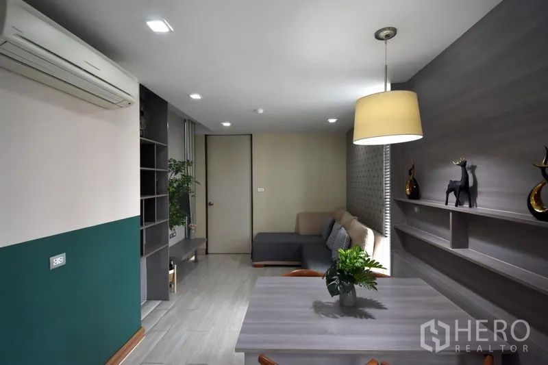 Condominium for rent in Khlong Toei, Bangkok - Dining nook with pendant light, floating shelves and an L-shaped sofa in the living area.