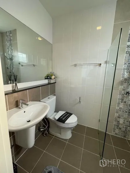 Detached House for rent or sale in Pathum Thani - Modern bathroom with glass shower, large mirror and wall tiles.