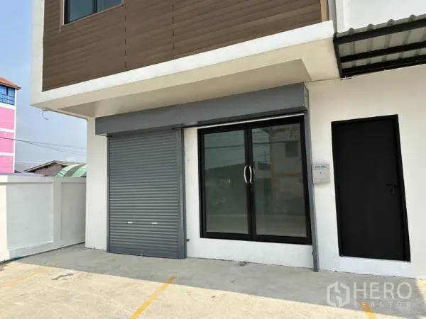 货栈 出租在Lam Luk Ka, Pathum Thani - 仓库前方办公室，设玻璃推拉门、卷闸门和划线停车位