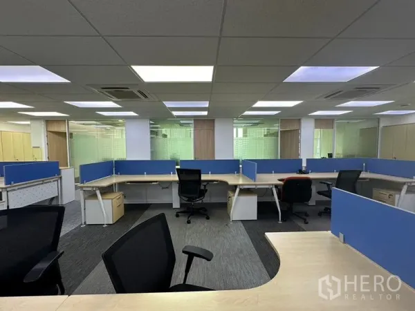 Office Space for rent - Cluster of L-shaped desks with blue dividers, ergonomic chairs, and glass-partitioned rooms.