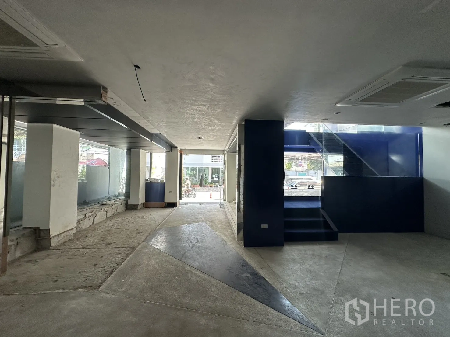 Retail Space for rent in Watthana, Bangkok - Deep retail hall leading toward a blue staircase and glass entrance, with mixed concrete and tile flooring.