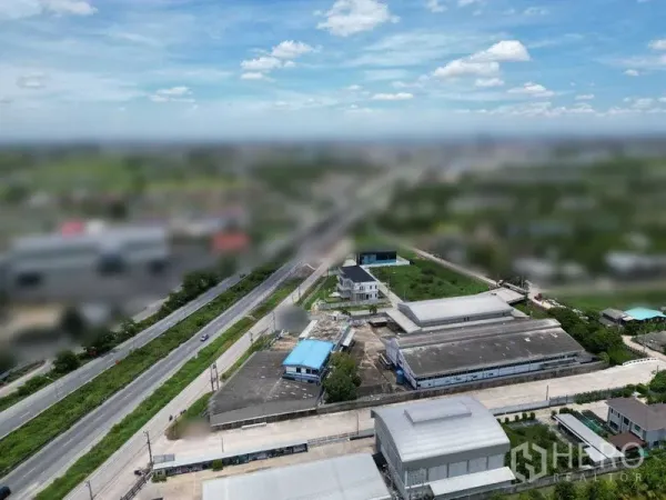 Land for sale in Bang Bua Thong, Nonthaburi - High-angle view showing a local arterial road with nearby factories, blue‑roofed buildings, and access roads across the countryside.