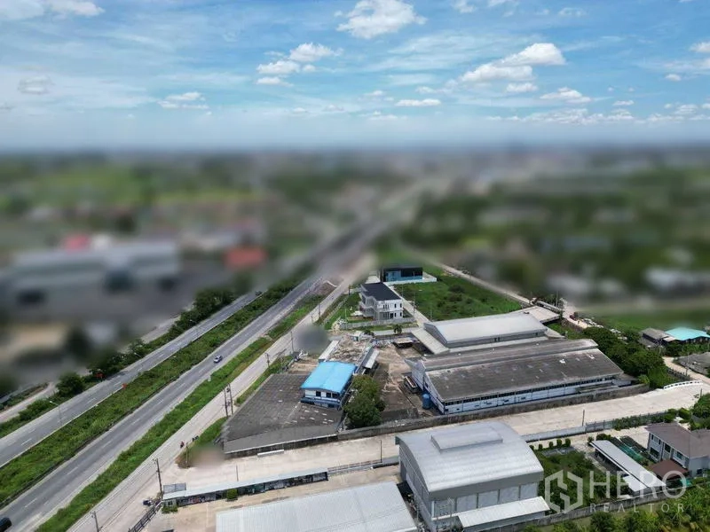 Land for sale in Bang Bua Thong, Nonthaburi - High-angle view showing a local arterial road with nearby factories, blue‑roofed buildings, and access roads across the countryside.