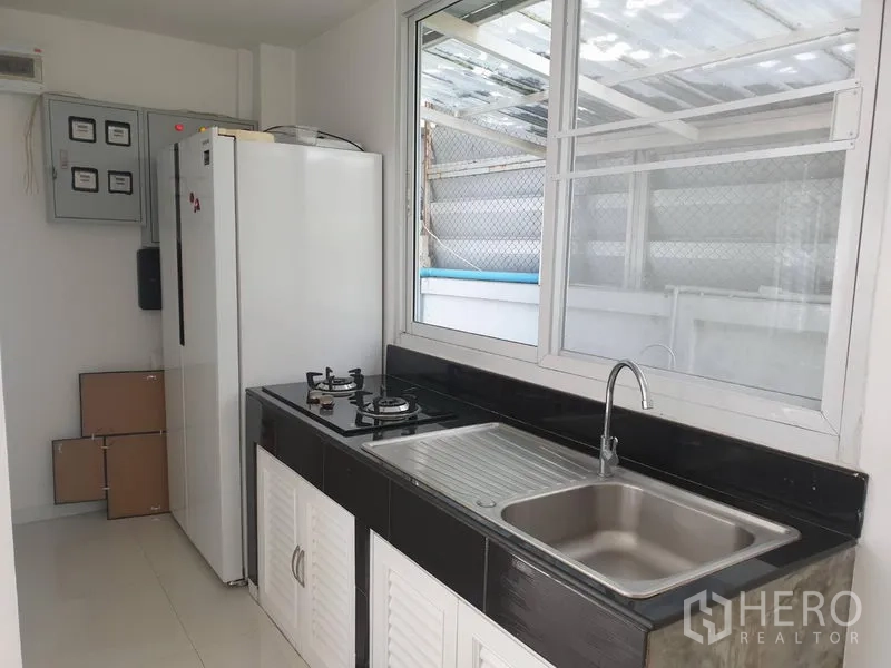 Detached House for rent in Khlong Toei, Bangkok - Light-filled kitchen with gas hob, sink, countertop and tall refrigerator by a window.