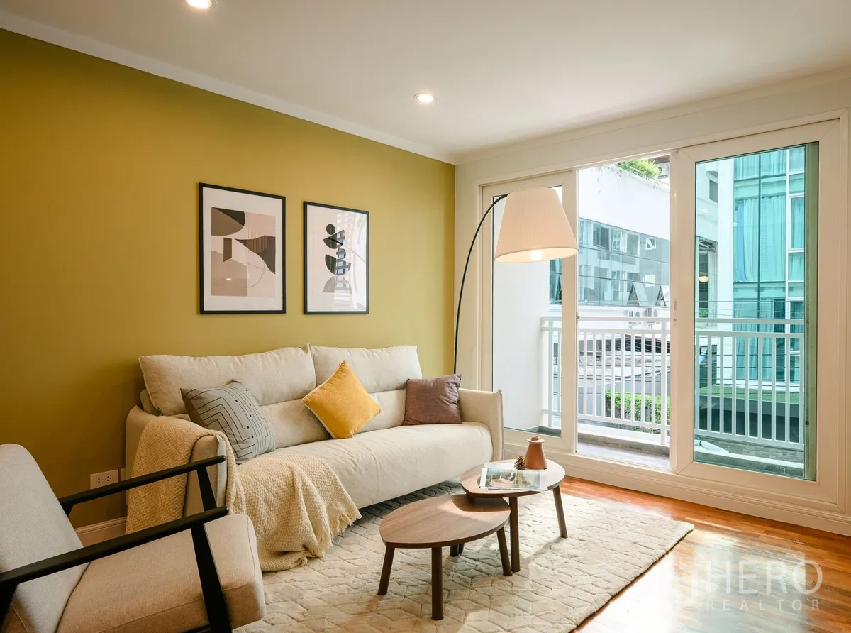 Condominium for sale in Watthana, Bangkok - Sofa beside floor-to-ceiling glass leading to a small balcony with exterior building view.