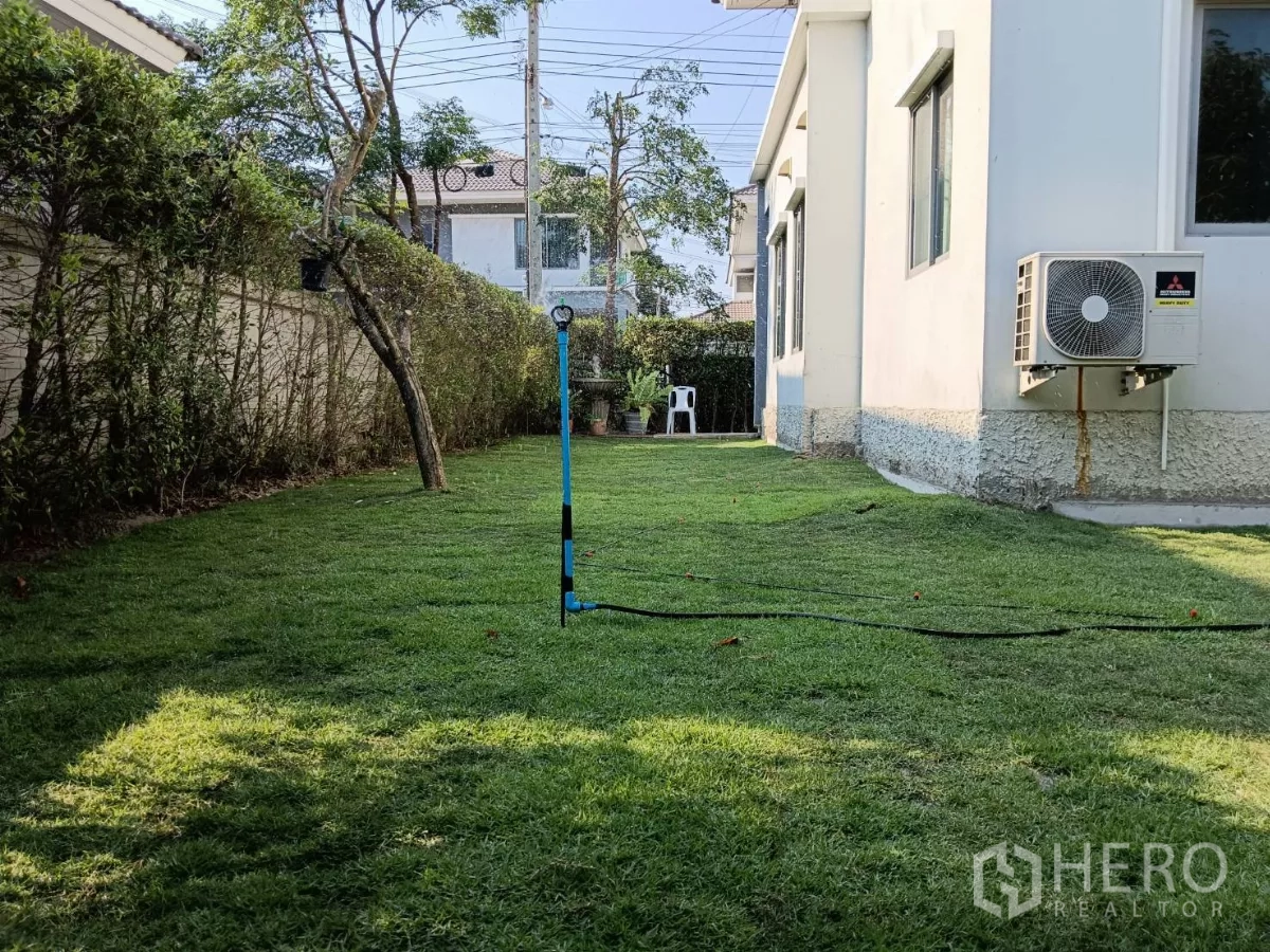 บ้าน ขายในLat Krabang, Bangkok - สนามหญ้าด้านข้าง มีแนวรั้วพุ่มไม้และคอมเพรสเซอร์แอร์