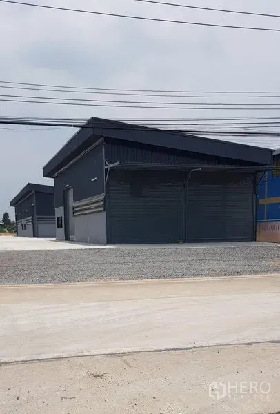 Warehouse for rent in Lat Lum Kaeo, Pathum Thani - Row of new dark-clad warehouse units with street frontage and power lines.
