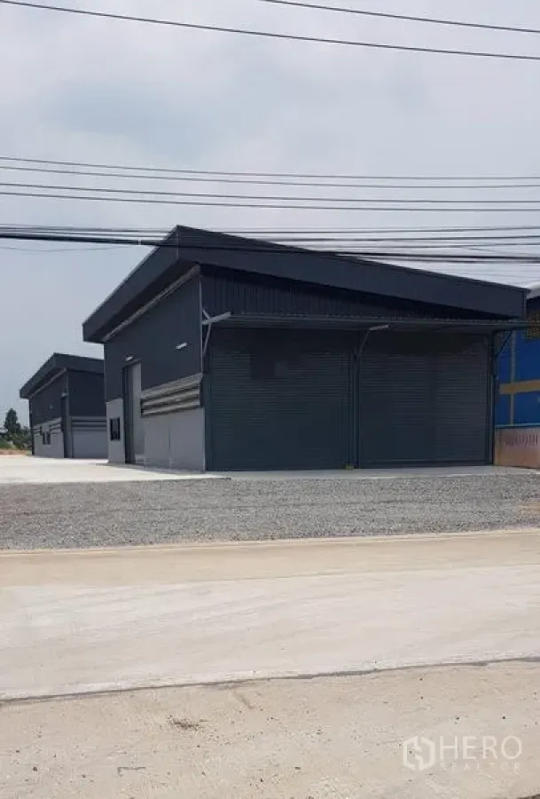 Warehouse for rent in Lat Lum Kaeo, Pathum Thani - Row of new dark-clad warehouse units with street frontage and power lines.