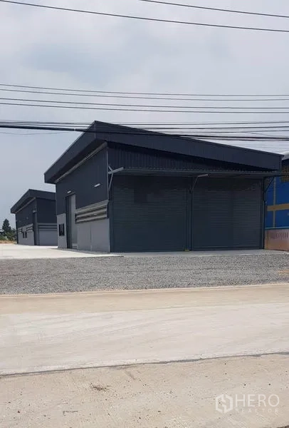 Warehouse for rent in Lat Lum Kaeo, Pathum Thani - Row of new dark-clad warehouse units with street frontage and power lines.