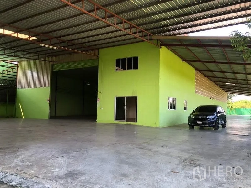 Factory for rent in Sam Khok, Pathum Thani - Front yard view with office block and wide shuttered entrance beneath a steel canopy.