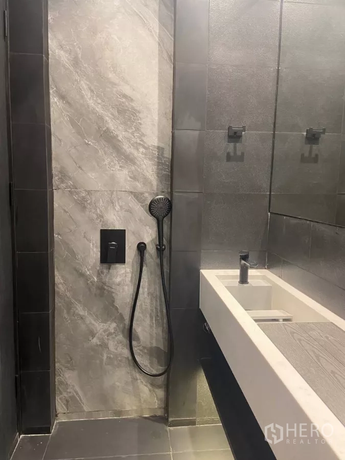 ทาวน์เฮาส์ ให้เช่าในHuai Khwang, Bangkok - ห้องน้ำสมัยใหม่ กระเบื้องเทา ชาวเวอร์มือถือ และอ่างล้างหน้ายาวสีขาว.