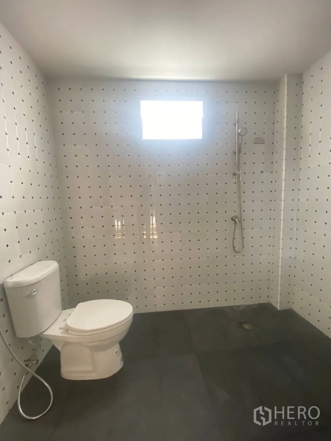 Home Office for sale - Spacious bathroom with toilet and shower against dotted white tiles.