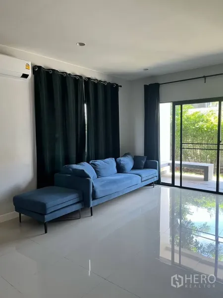 บ้าน ให้เช่าหรือขายในLam Luk Ka, Pathum Thani - ห้องนั่งเล่นสว่าง โซฟาสีน้ำเงิน พื้นแกรนิตเงา และประตูกระจกบานเลื่อนออกสู่เฉลียง