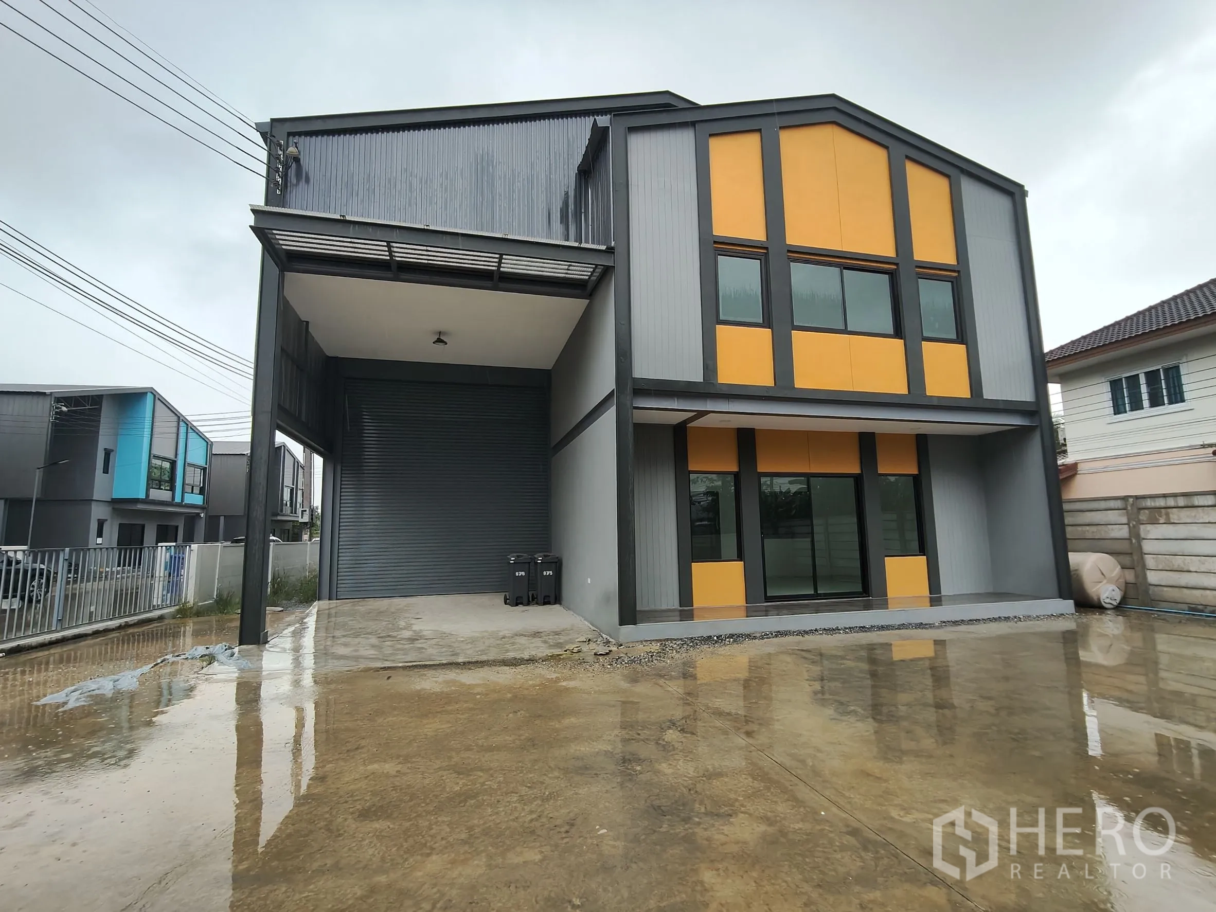 คลังสินค้า ให้เช่าหรือขายในBang Yai, Nonthaburi - ด้านหน้าโกดังสมัยใหม่โทนเทา‑ส้ม พร้อมออฟฟิศสองชั้น หลังคาลานโหลด ประตูม้วน และลานคอนกรีตกว้าง