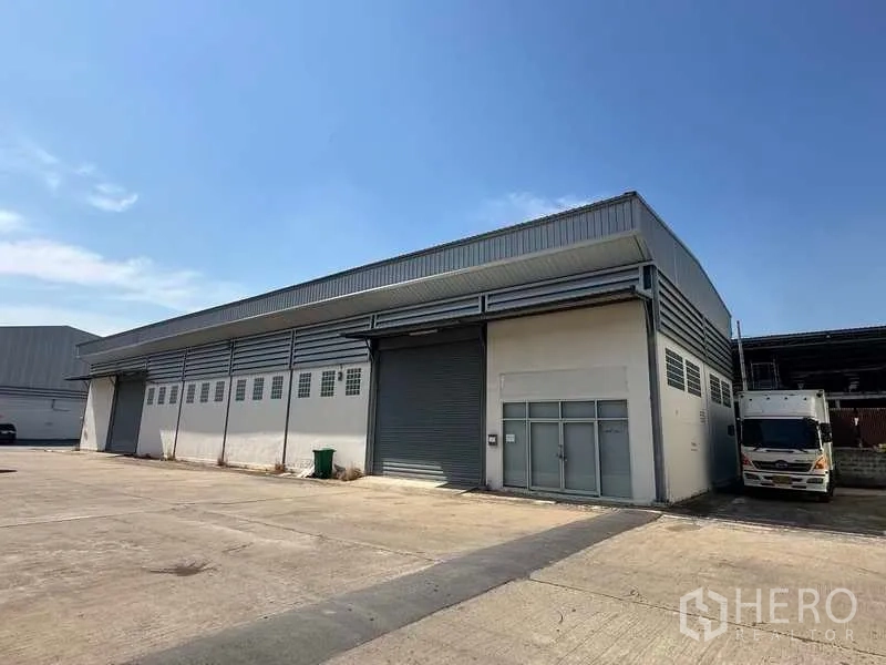 货栈 出租在Bang Bua Thong, Nonthaburi - 正立面展示主卷闸门及玻璃幕办公区