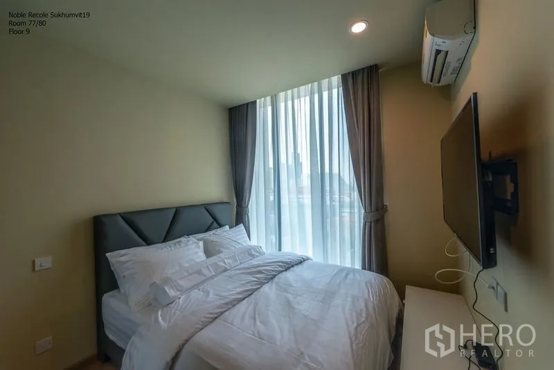 Condominium for rent in Watthana, Bangkok - Bedroom with large window, wall-mounted TV and air-conditioning overlooking the city.