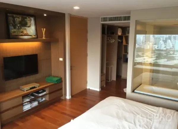 公寓 出租或出售在Sathon, Bangkok - 沙吞公寓卧室，木地板、嵌入式电视墙与步入式衣柜，玻璃隔断浴室可观曼谷天际线。