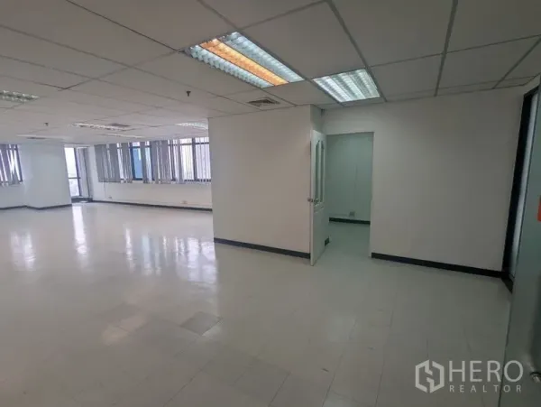 สำนักงาน ให้เช่าหรือขาย - สำนักงานพื้นที่เปิดโล่ง พื้นกระเบื้อง ฝ้าเพดานทีบาร์ ไฟฟลูออเรสเซนต์ และประตูสู่ห้องส่วนตัว พร้อมหน้าต่างบานยาวมีม่าน