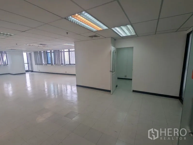สำนักงาน ให้เช่าหรือขาย - สำนักงานพื้นที่เปิดโล่ง พื้นกระเบื้อง ฝ้าเพดานทีบาร์ ไฟฟลูออเรสเซนต์ และประตูสู่ห้องส่วนตัว พร้อมหน้าต่างบานยาวมีม่าน
