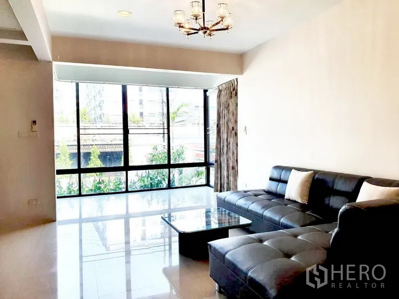 บ้าน ให้เช่าในPhra Khanong, Bangkok - ห้องนั่งเล่นสว่าง โซฟาหนังตัวแอล โคมไฟ และหน้าต่างกระจกเต็มผนัง