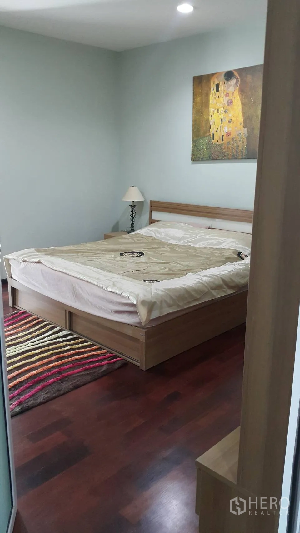 Condominium for rent in Watthana, Bangkok - Master bedroom with wooden bed frame, bedside lamp, colorful rug and wall art.