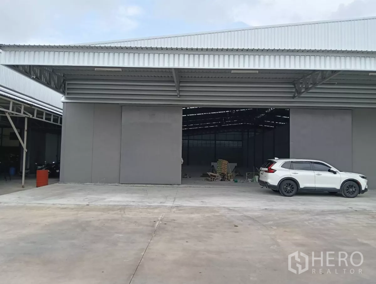Warehouse for rent in Samut Prakan - Modern warehouse exterior with large sliding doors, a wide concrete yard and an SUV parked in front.