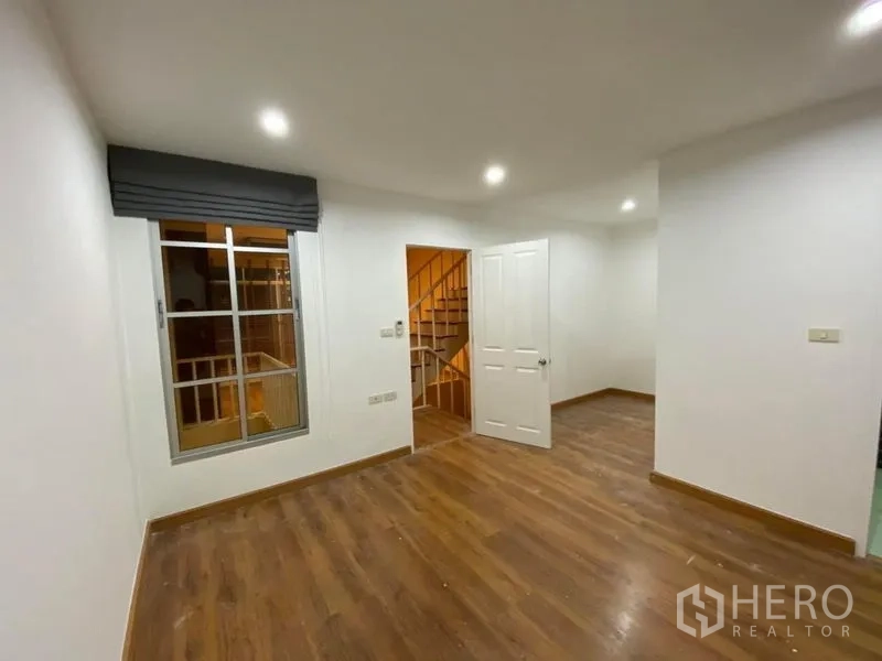 联排别墅 出租在Lat Phrao, Bangkok - 明亮卧室，木地板、窗户与通往楼梯平台的门。