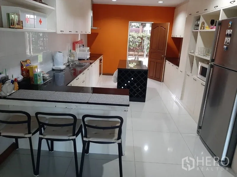 Home Office for sale in Phra Khanong, Bangkok - Spacious modern kitchen with white cabinetry, bar seating and an orange feature wall.