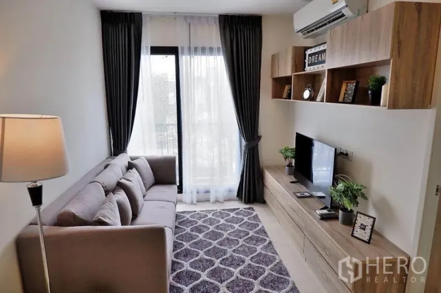 Condominium for rent in Huai Khwang, Bangkok - Living room facing the balcony with air conditioning and built-in wood storage.