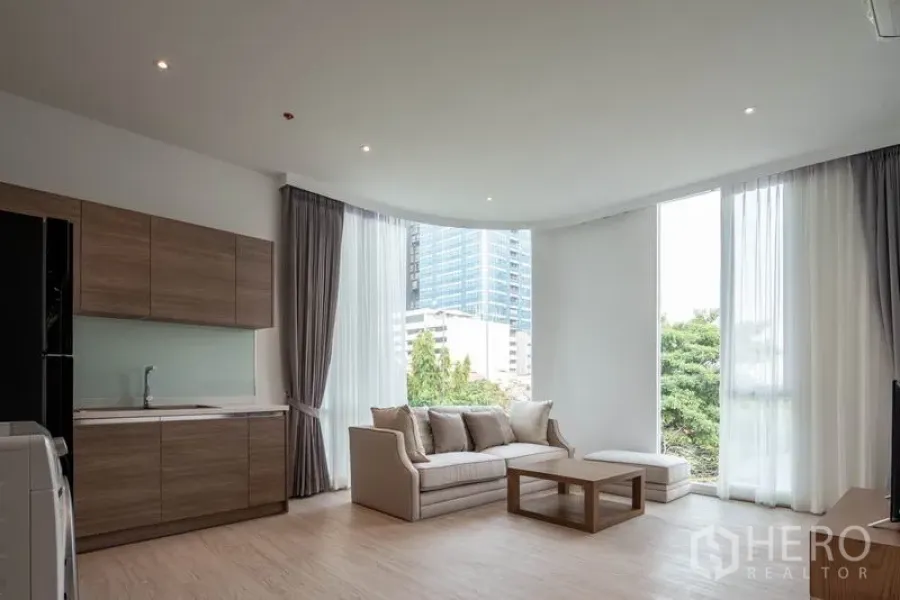 คอนโด ให้เช่าในKhlong Toei, Bangkok - ห้องนั่งเล่นแบบโอเพนสเปซสว่าง โปร่ง พร้อมครัวบิลท์อิน โซฟา และหน้าต่างเต็มผนังมองเห็นต้นไม้และเมือง