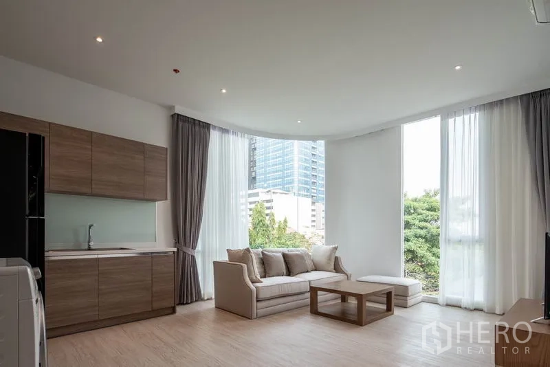 คอนโด ให้เช่าในKhlong Toei, Bangkok - ห้องนั่งเล่นแบบโอเพนสเปซสว่าง โปร่ง พร้อมครัวบิลท์อิน โซฟา และหน้าต่างเต็มผนังมองเห็นต้นไม้และเมือง