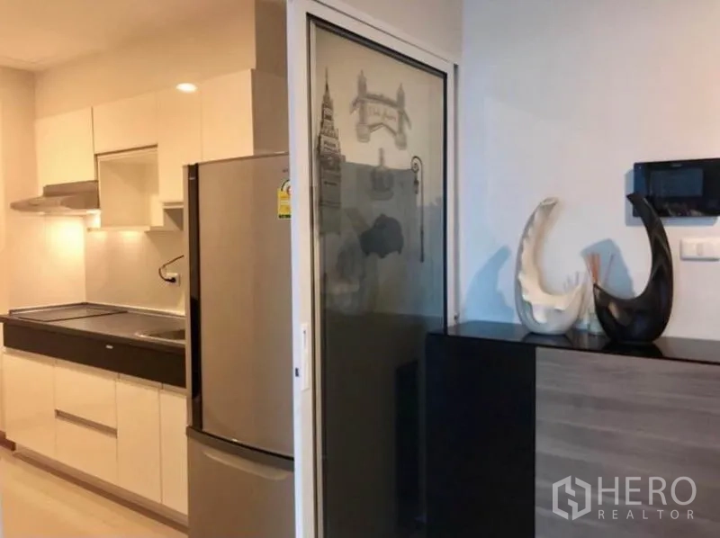 คอนโด ให้เช่าในBangkok - ครัวปิดโทนขาวพร้อมตู้เก็บของ เครื่องดูดควัน และตู้เย็นสแตนเลส หลังประตูกระจกบานเลื่อน