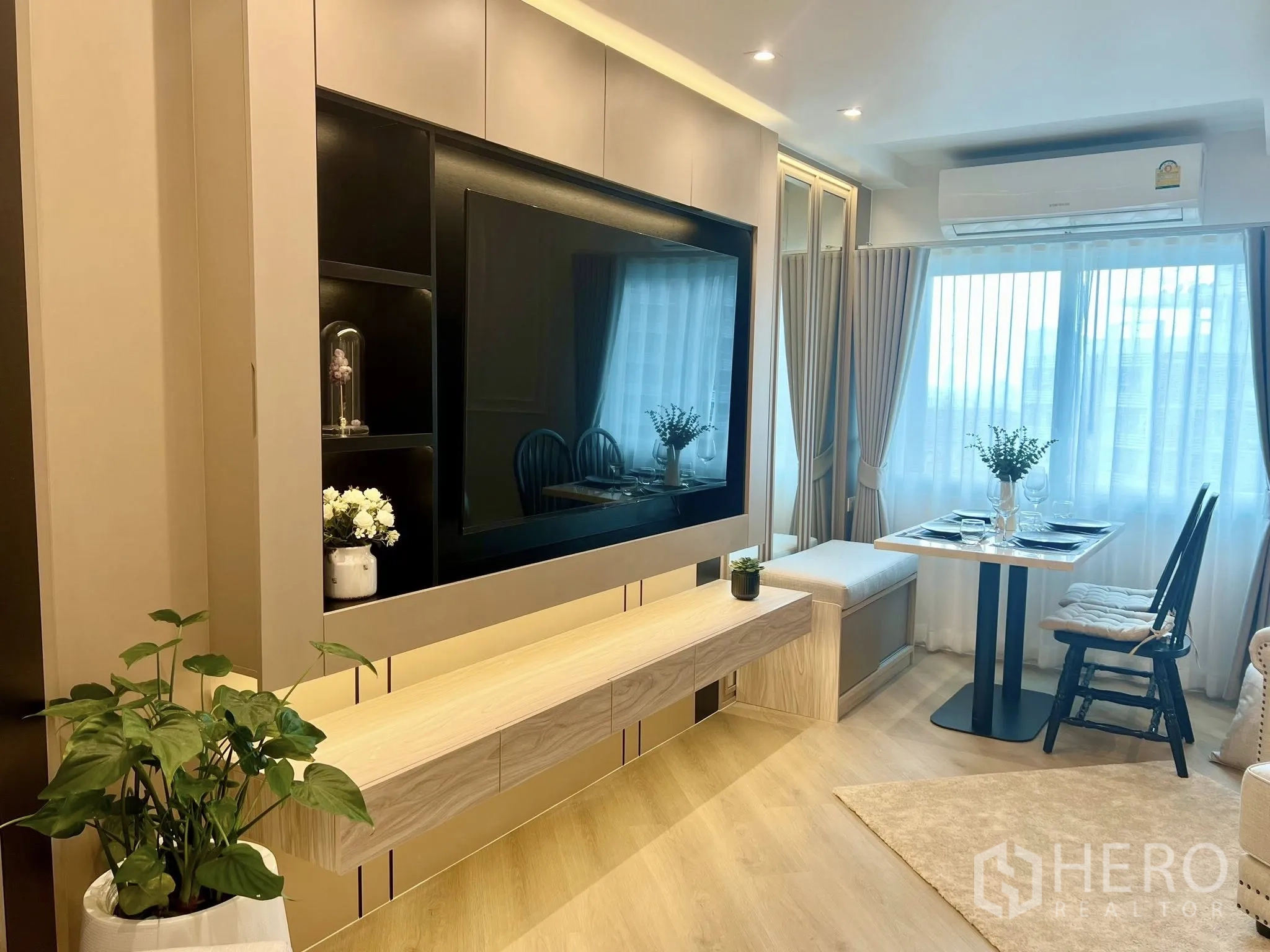Condominium for rent or sale in Yan Nawa, Bangkok - TV feature wall facing a small dining nook beside wide windows with sheer drapes.