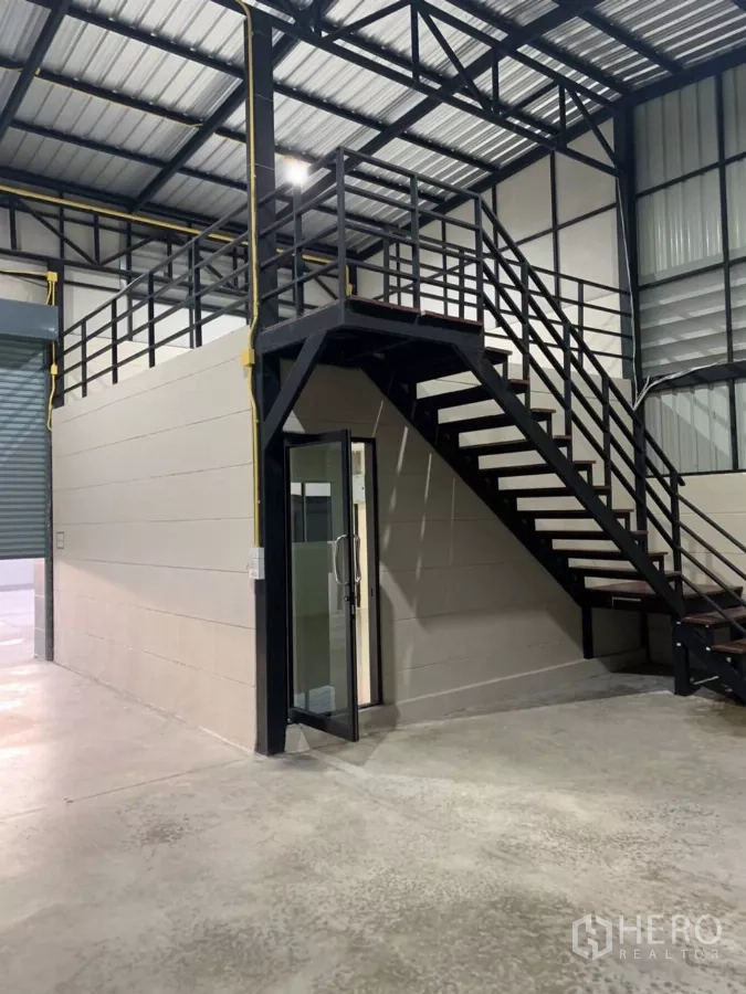货栈 出租在Bang Bua Thong, Nonthaburi - 仓库内部设钢制楼梯通往夹层，玻璃门办公室，高挑金属屋顶与混凝土地面。