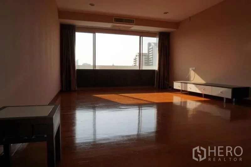 Condominium for rent in Watthana, Bangkok - Large living area with wall‑to‑wall windows, shining wood floors and low TV console.