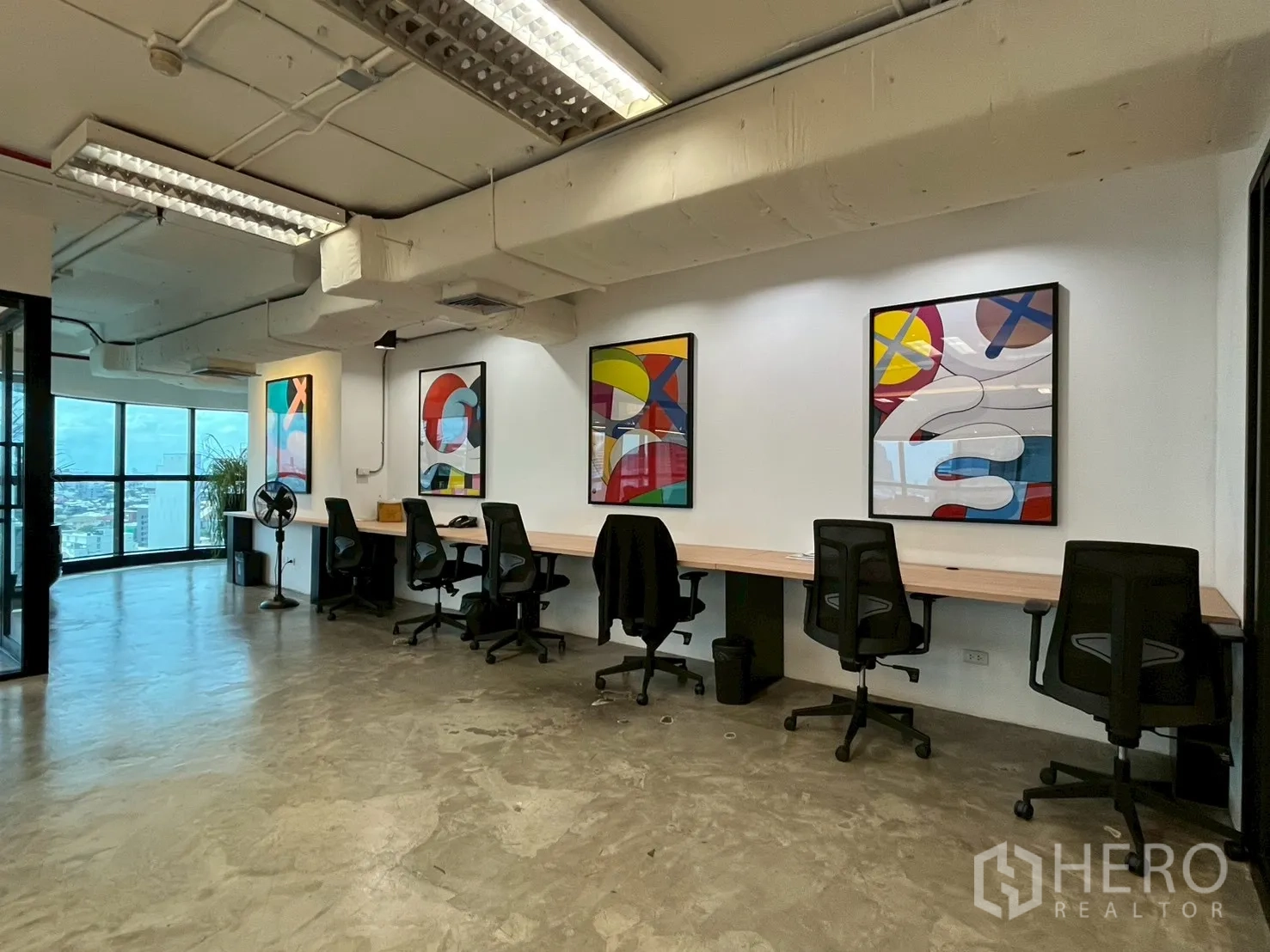 办公室 for rent in Watthana, Bangkok - 一排工位与办公椅，墙面彩色艺术画，水泥地面。