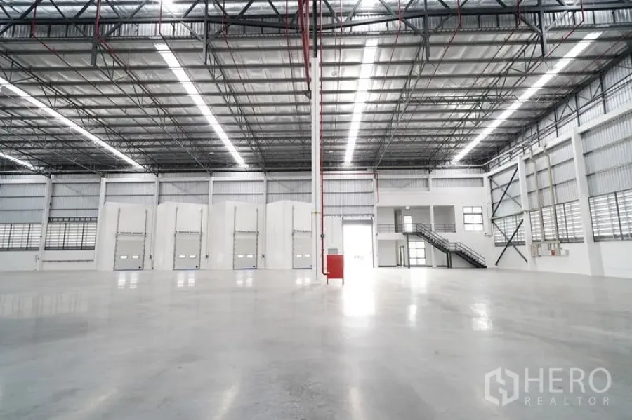 Warehouse for rent in Khlong Luang, Pathum Thani - Wide warehouse view with several loading bays, mezzanine office block, and staircase access.