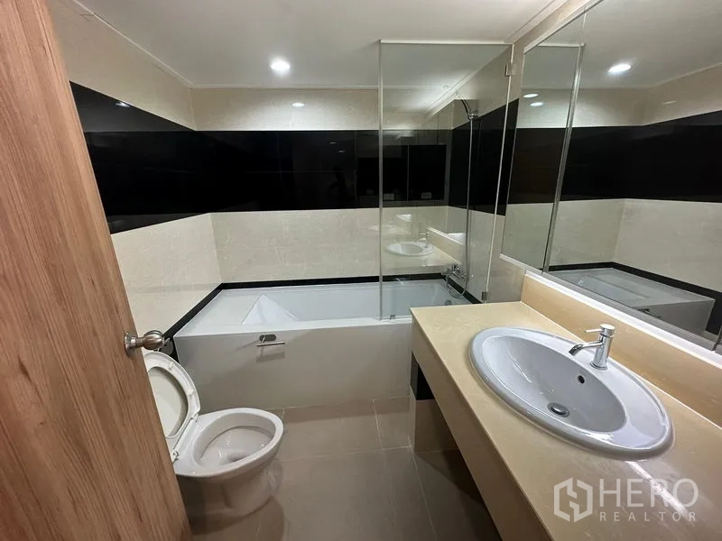 คอนโด ให้เช่าในWatthana, Bangkok - ห้องน้ำที่สองพร้อมอ่างอาบน้ำ ฉากกั้นกระจก กระเบื้องโทนอบอุ่น และอ่างล้างหน้าเคาน์เตอร์กว้าง