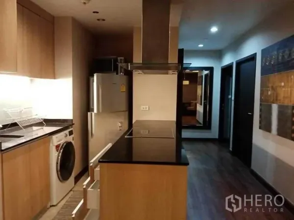 公寓 出租在Sathon, Bangkok - 走廊式厨房，黑色花岗岩台面，电磁炉与烟机，冰箱及洗衣机，通向卧室区。