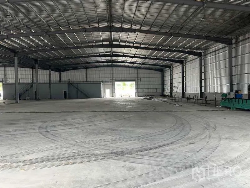 工厂 出租在Rayong - 大型厂房大厅，光滑混凝土地面，后部卷帘门与内部办公区。