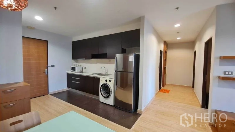 Condominium for rent or sale in Watthana, Bangkok - Compact kitchen with upper and lower cabinets, stainless sink, appliances, and view to the hallway.