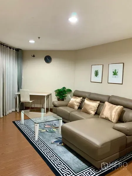 Condominium for rent in Huai Khwang, Bangkok - Open living area featuring sectional sofa, study desk by the window and decorative plants.