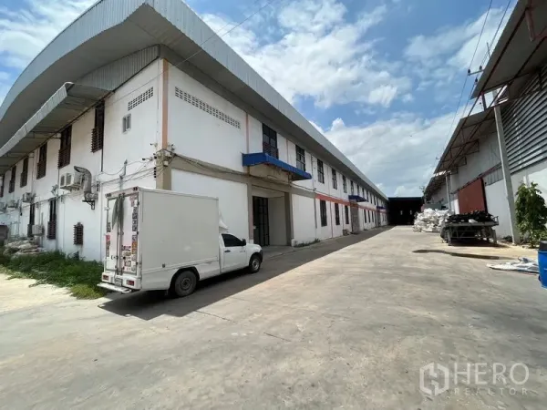 Warehouse for rent in Nakhon Chai Si, Nakhon Pathom - High-roof warehouse with blue awnings and a long paved loading driveway, small box truck parked in Nakhon Chai Si.