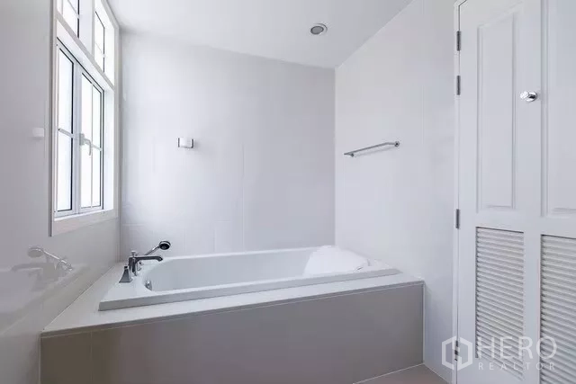 Townhouse for rent in Watthana, Bangkok - Bathroom with built-in bathtub, window and clean white tile walls.