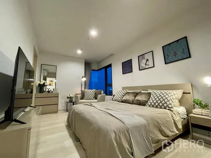 Condominium for rent in Pathum Wan, Bangkok - Primary bedroom at night with upholstered bed, TV and corner windows overlooking city lights.