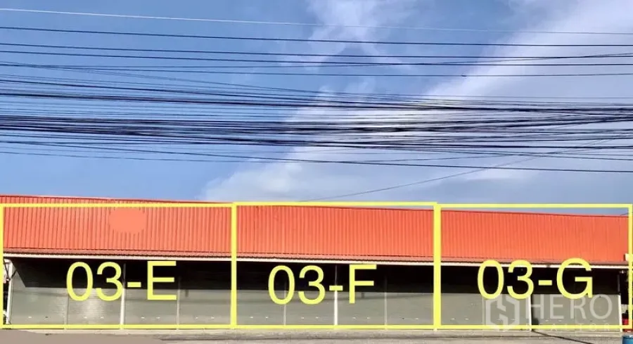货栈 出租在Pathum Thani - 橙色屋顶的连排仓库，正面设多组卷帘门，标注03‑E、03‑F、03‑G，门前面宽充足。