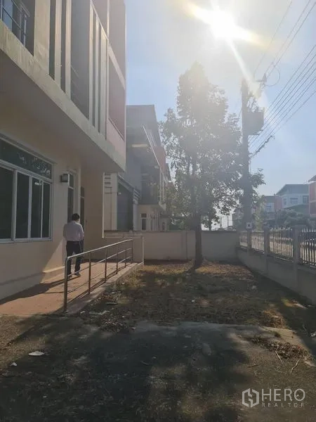 โรงงาน ให้เช่าหรือขายในLam Luk Ka, Pathum Thani - ลานหน้าบ้าน ทางเดิน ต้นไม้ และรั้วโครงการภายใต้แสงแดดยามบ่าย
