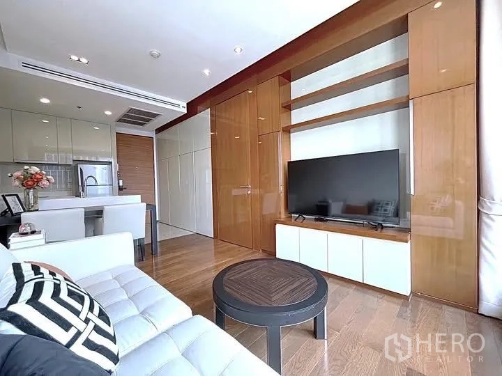 Condominium for rent in Khlong Toei, Bangkok - Open-plan living area with TV wall, glossy wood cabinetry, island dining counter, and wood flooring.