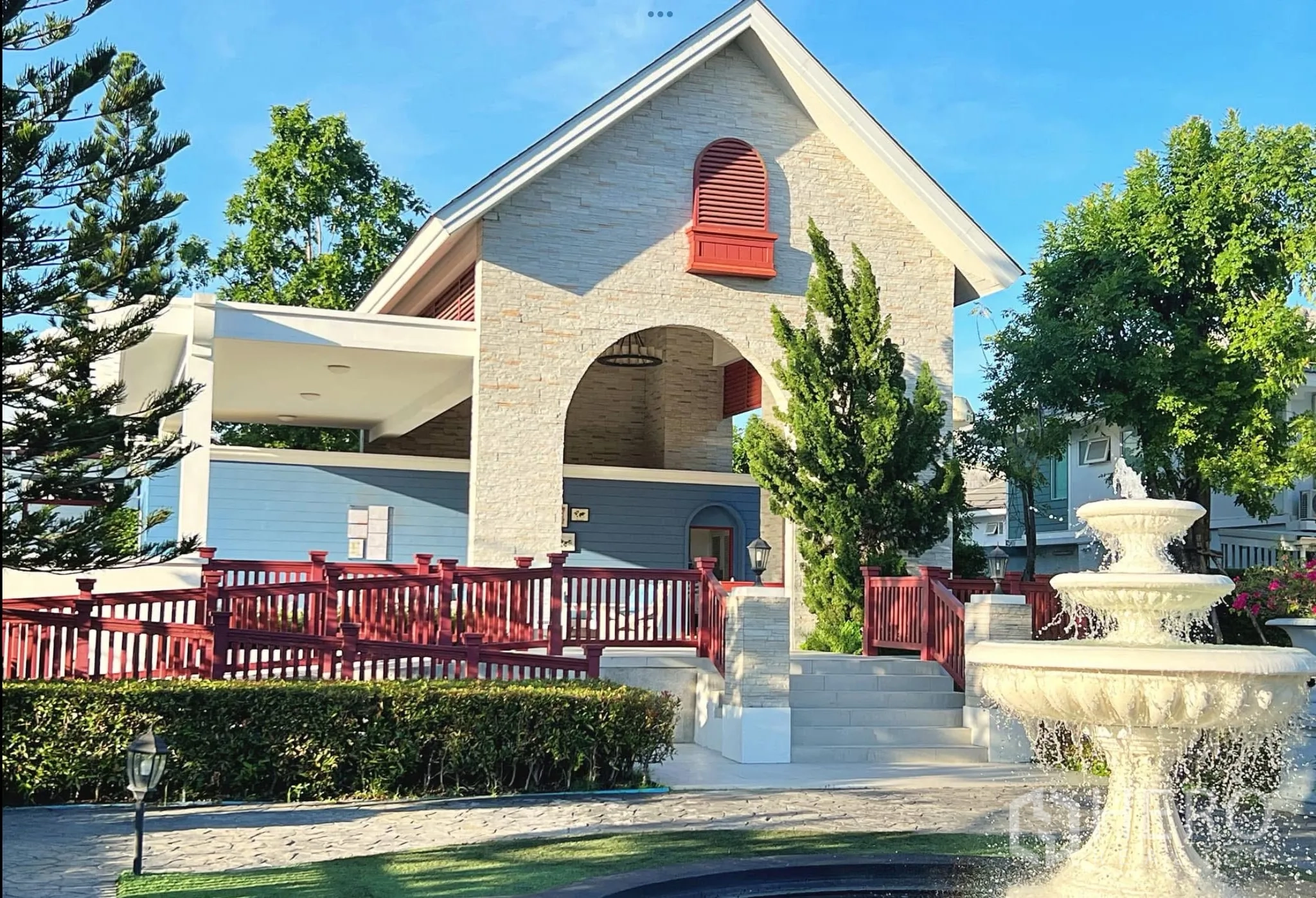 Townhouse for rent or sale in Sai Mai, Bangkok - Clubhouse façade with red railings, stone arch and tiered fountain.